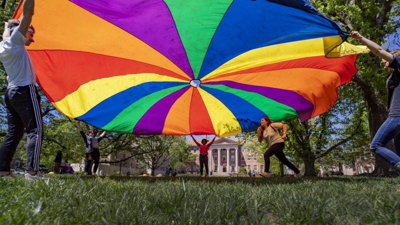 Students run under rainbow parachute during LGBTQ program on the quad