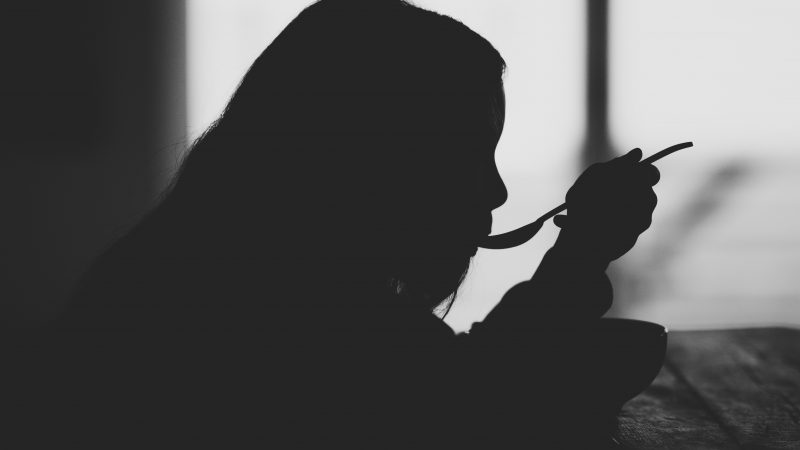 Silhouetted person with spoon in mouth