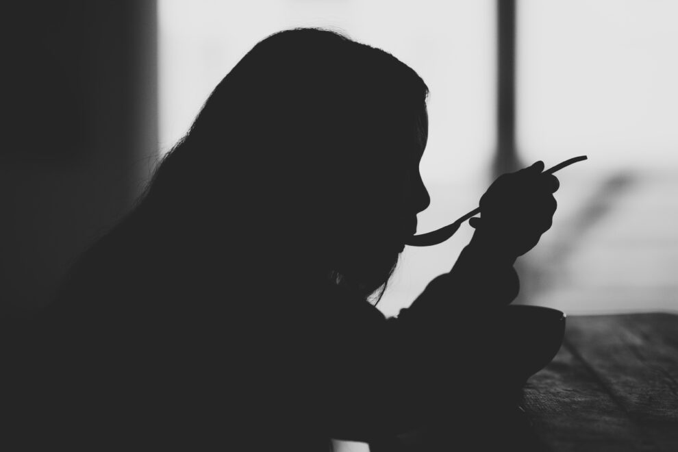 Silhouetted person with spoon in mouth