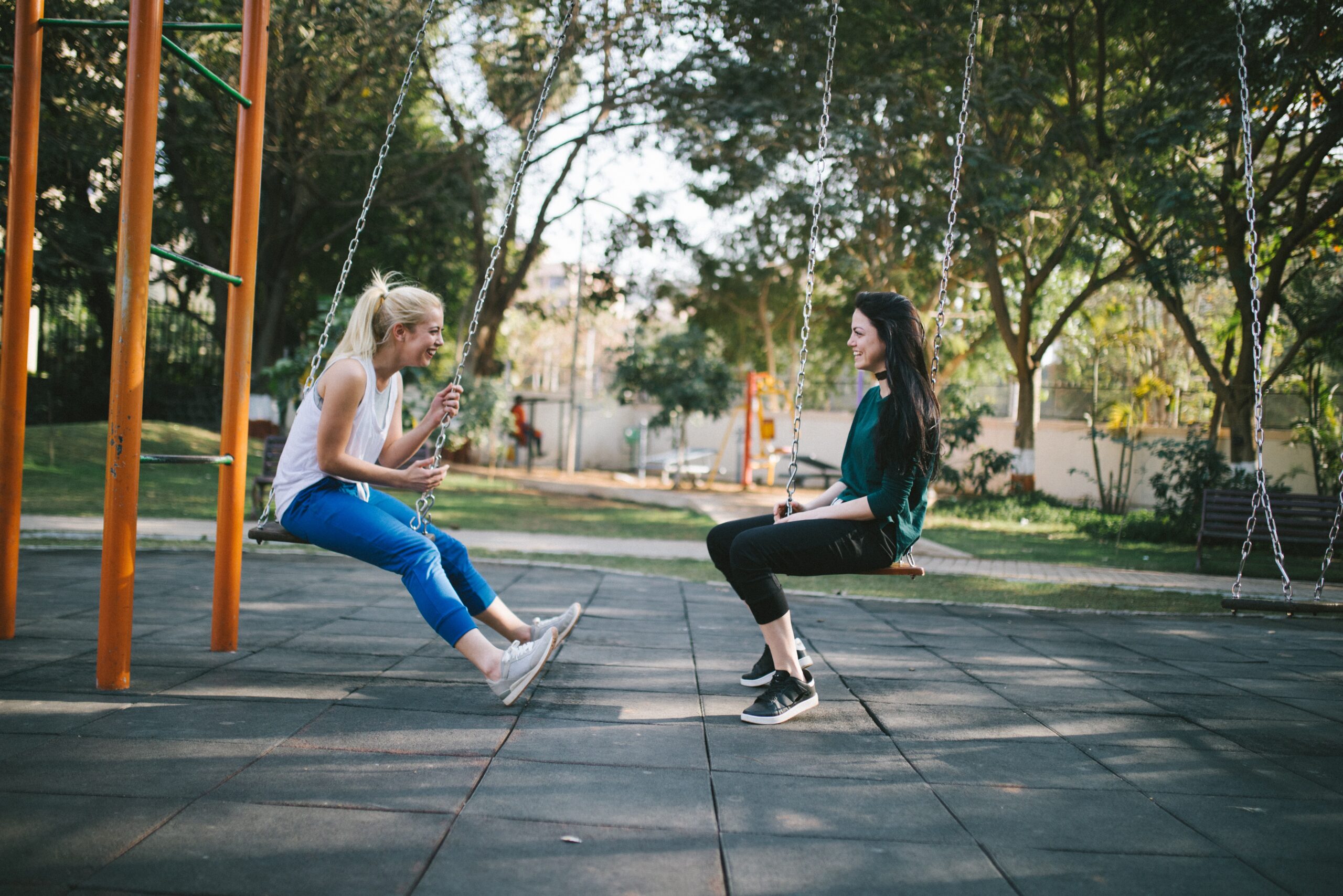 two women sit on swings smiling at each other