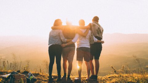 4 people with arms around each other watch the sunset