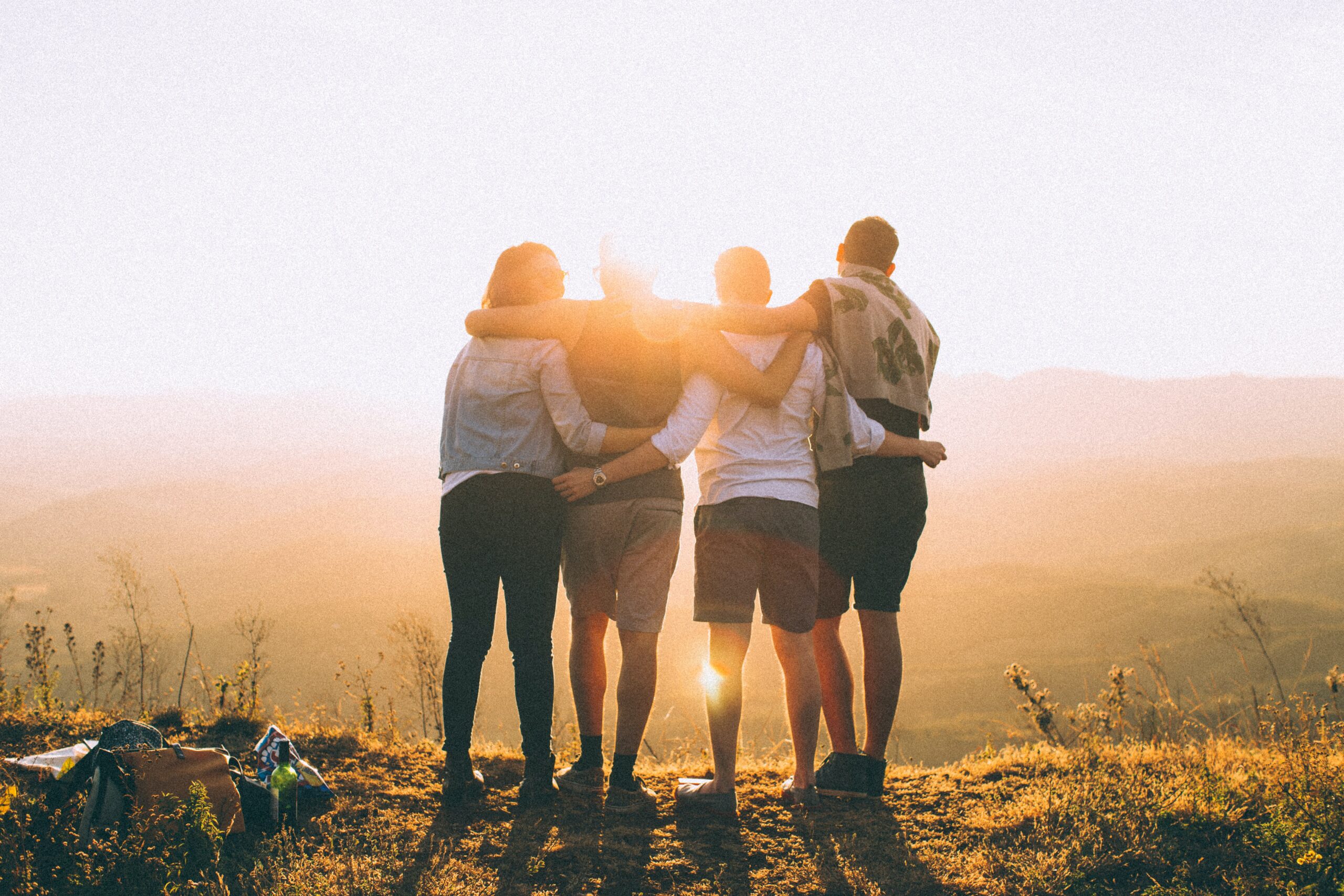 4 people with arms around each other watch the sunset