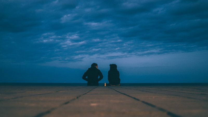 Two people talk under a cloudy sky