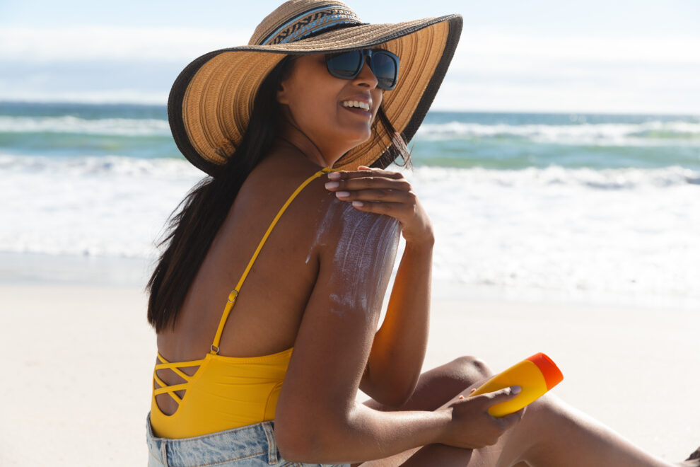 Smiling mixed race woman on beach using sunscreen cream
