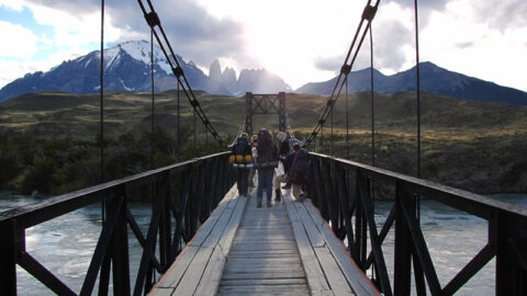 Students walking on a bridge across a river. Mountains visible in the background.