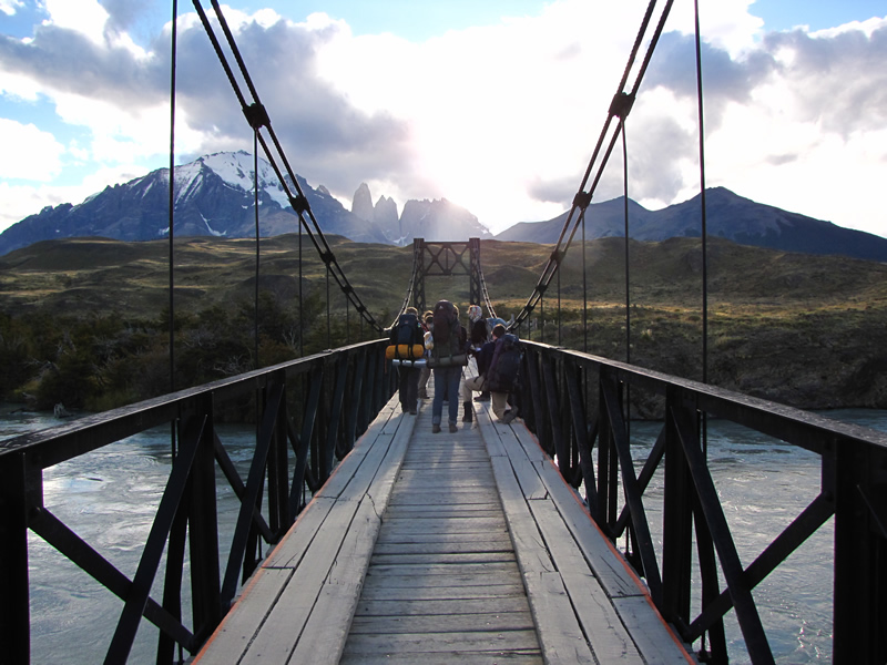 Students walking on a bridge across a river. Mountains visible in the background.